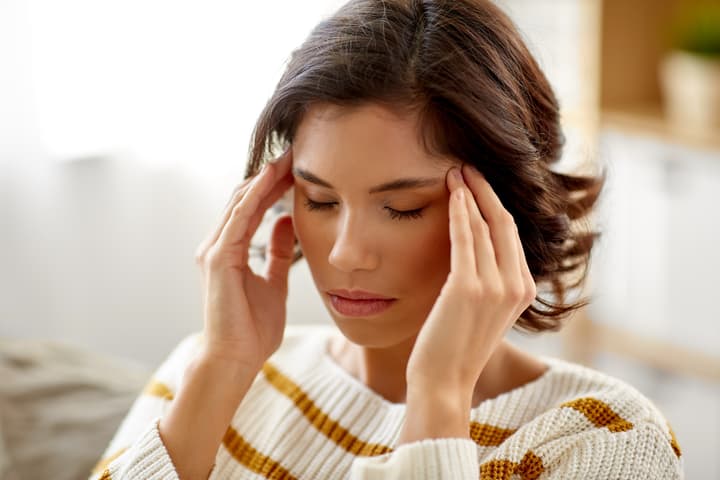 a woman with closed eyes gently holds her temples, appearing to be dealing with feelings of stress
