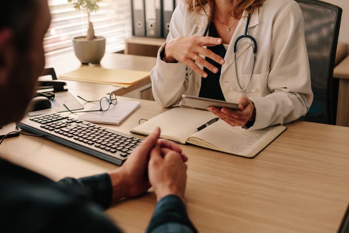 A doctor reviews information on a tablet with a patient during an office visit
