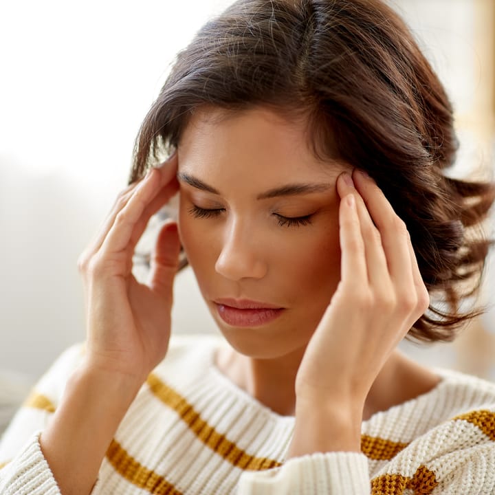a woman with closed eyes gently holds her temples, appearing to be dealing with feelings of stress