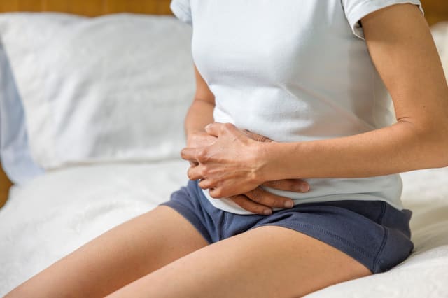 a woman, sitting on a bed, holding her stomach
