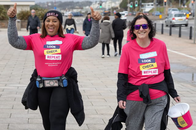 Two people in pink ABC Jersey shirts walking with collection buckets.