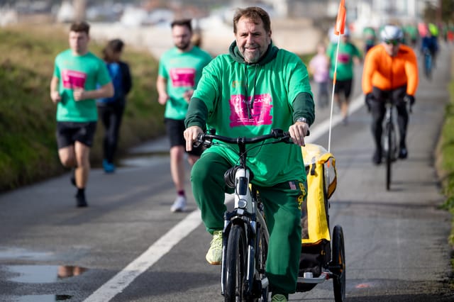 A cyclist in a green Medicann event shirt taking part alongside runners.