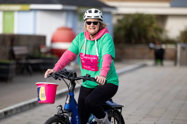 A cyclist in a green Medicann event shirt carrying a collection bucket.